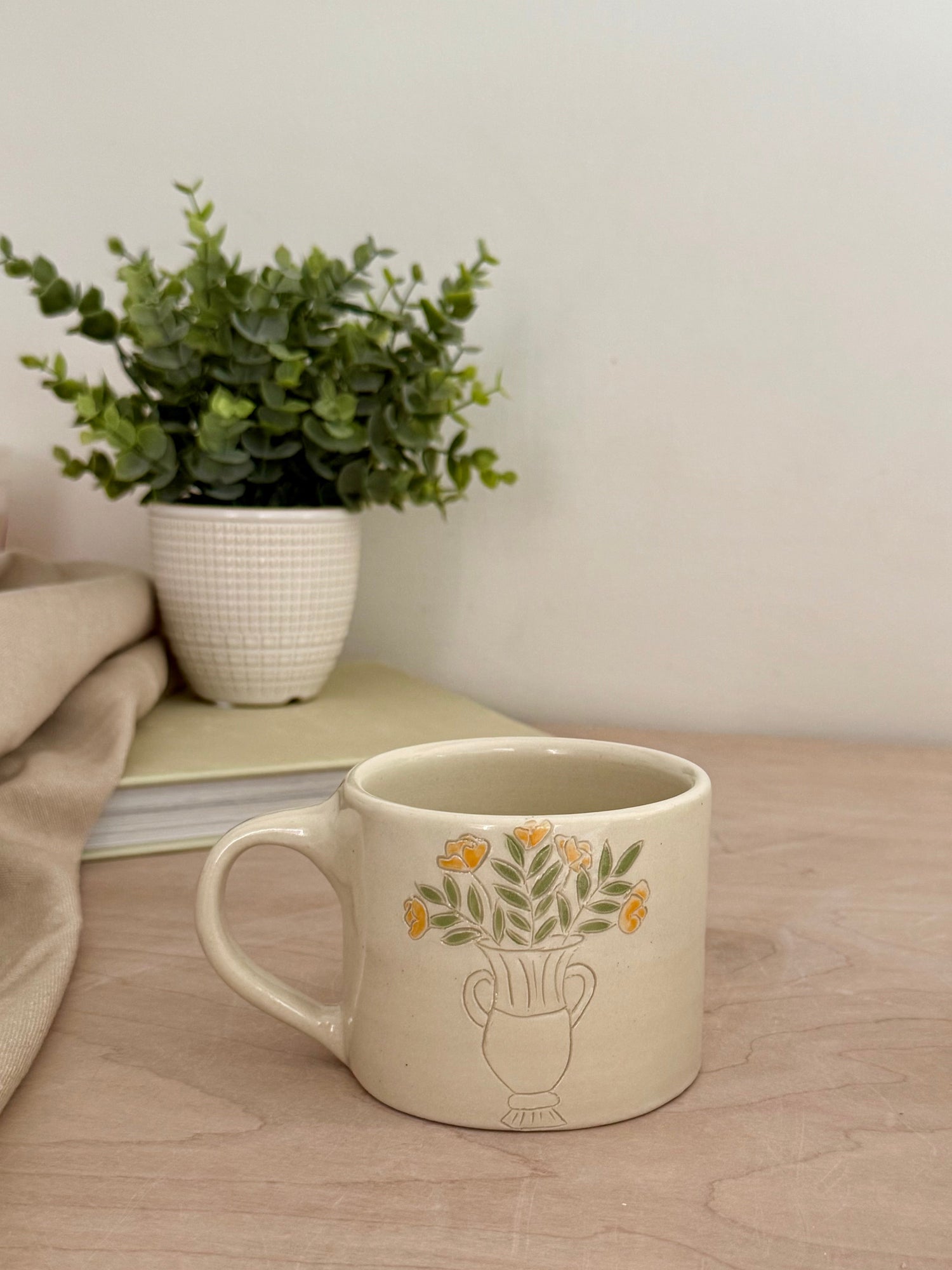 Hand holding handmade cream stoneware mug showing hand-carved yellow rose bouquet detail