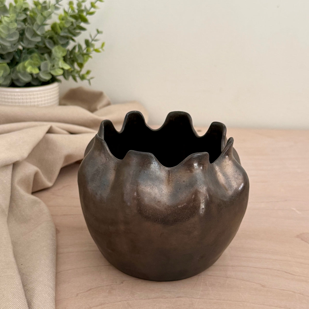 Handmade stoneware ruffle rim vase in deep bronze-black glaze on wood surface